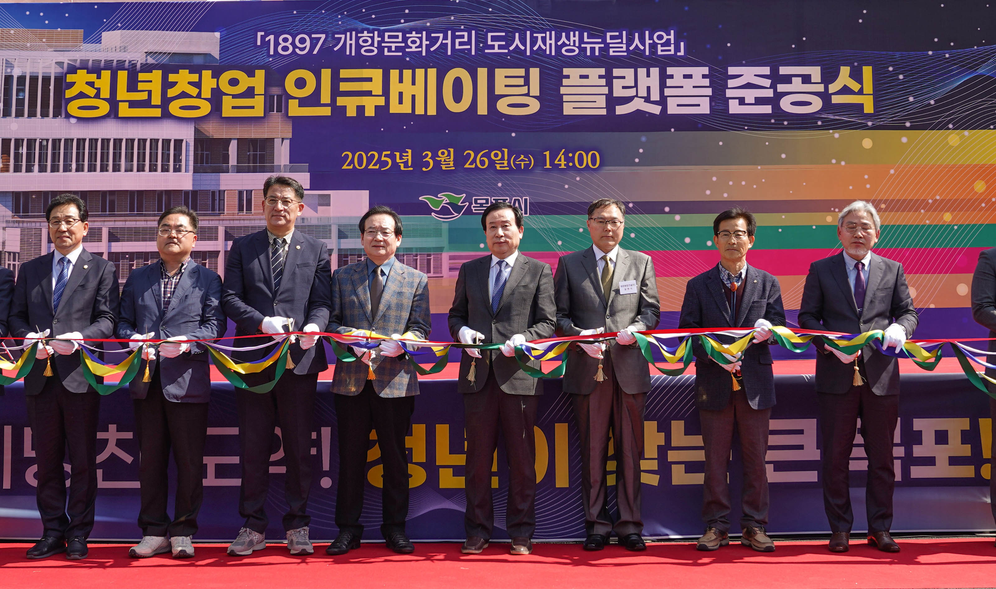 ‘청년창업 인큐베이팅 플랫폼 준공식’ 무대 위에서 진행된 테이프 커팅식. 정장을 입은 박홍률 목포시장을 비롯한 8명의 인사들이 다채로운 색상의 리본을 잡고 일렬로 서 있으며, 배경에는 '청년창업 인큐베이팅 플랫폼 준공식'이라는 큰 글씨와 '2025년 3월 26일(수) 14:00'라는 날짜, 목포시 로고, 건물 일러스트가 보인다.
