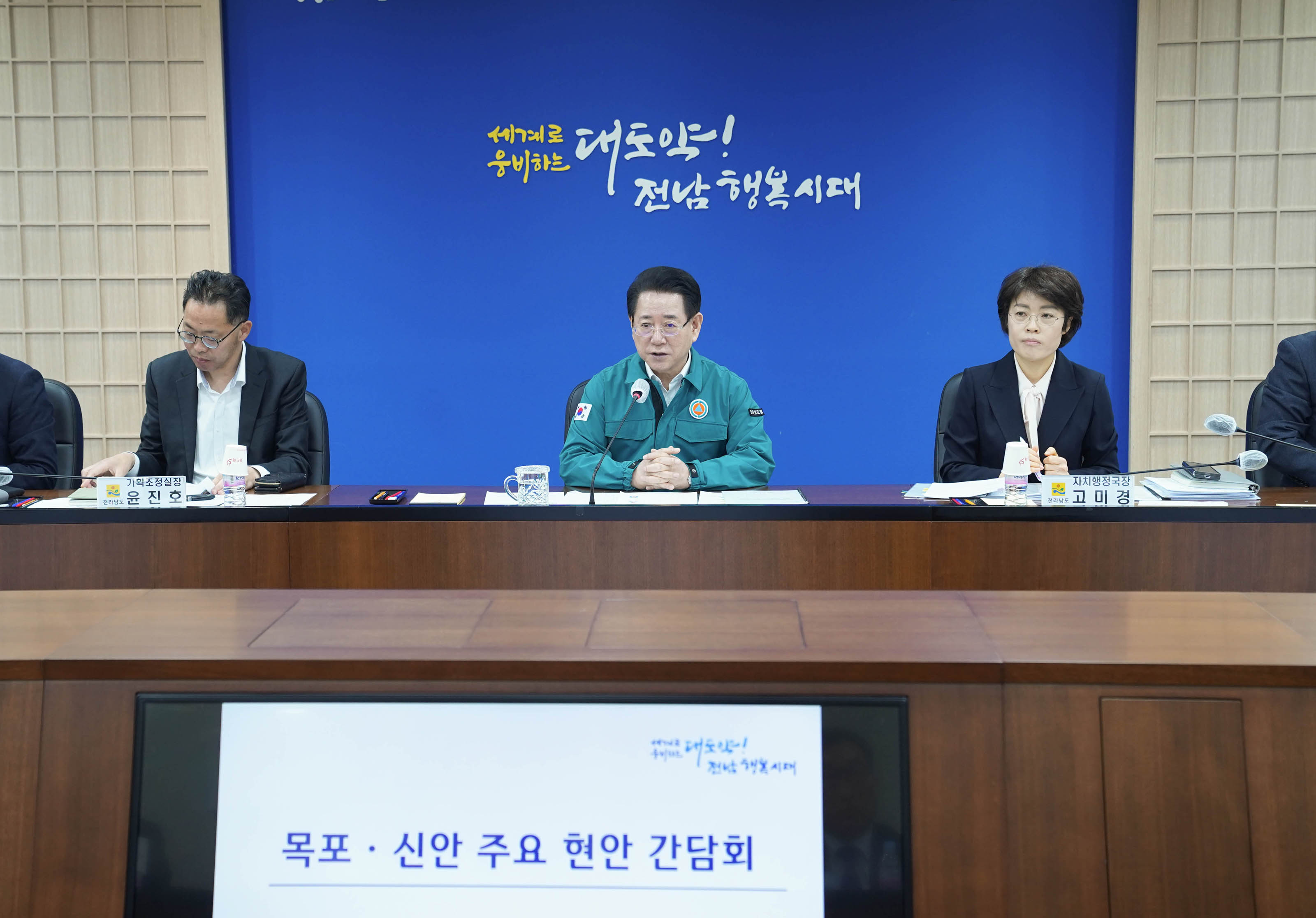 전라남도청 회의실에서 김영록 전라남도지사를 중심으로 열린 '목포·신안 주요 현안 간담회'에서 관계자들의 발언을 듣고 있다.
김영록 전라남도지사의 오른쪽에는 고미경 자치행정국장이, 왼쪽에는 윤진호 기획조정실장이 각각 이름표와 함께 앉아 있다. 배경에는 '세계로 웅비하는 대도약! 전남 행복시대'라는 문구가 파란색 벽면에 적혀 있다.
