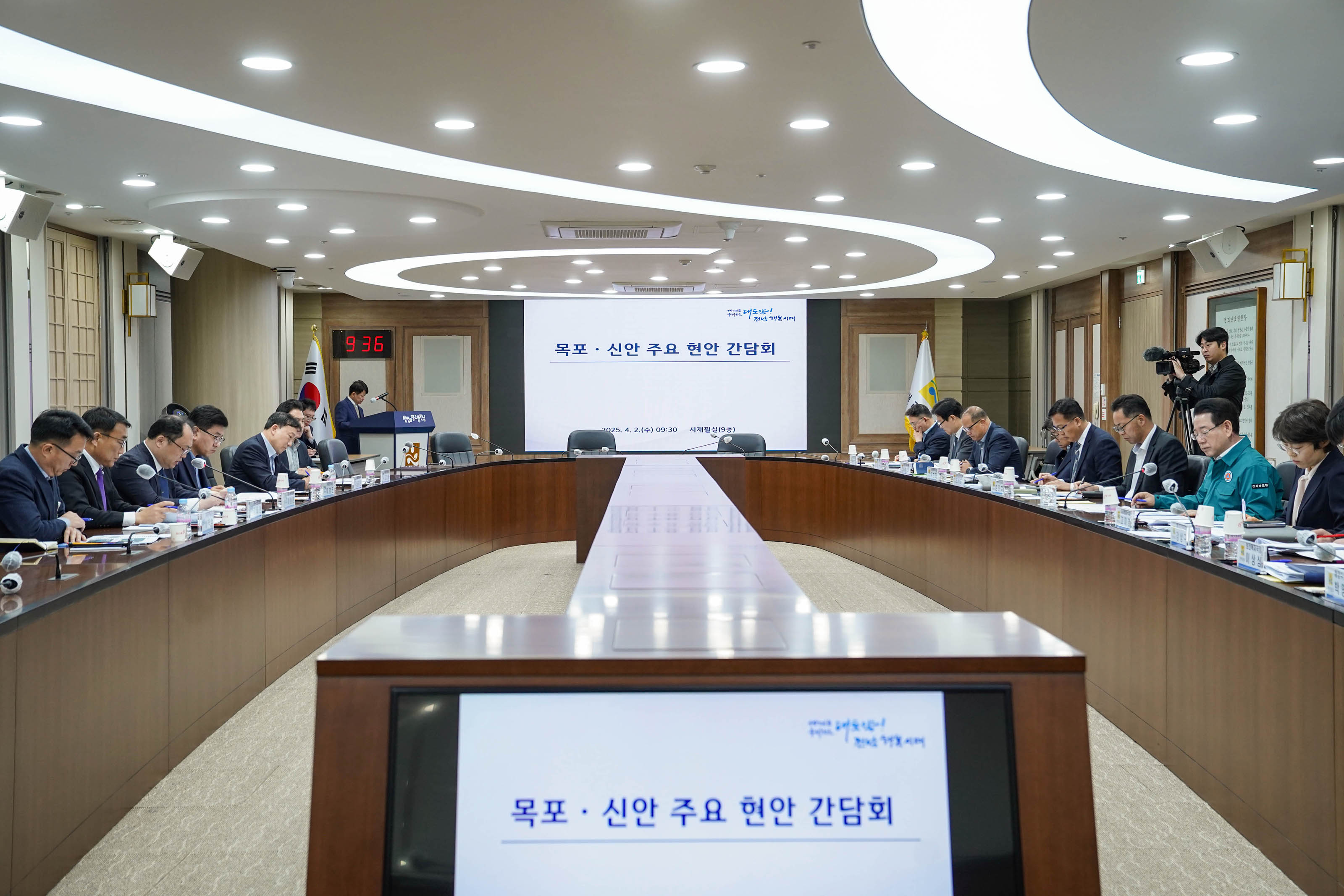 전라남도청 회의실에서 열린 '목포·신안 주요 현안 간담회' 모습. 회의실 중앙 정면 스크린에는 '목포·신안 주요 현안 간담회', 하단에는 '2025. 4. 2.(화) 09:30' 이라는 문구가 표시되어 있다. 회의 좌측과 우측에 앉은 각 기관 관계자들이 자료를 검토하고 발언을 준비하고 있다. 왼쪽 뒤편에는 촬영 중인 카메라맨과 발표자가 보인다.