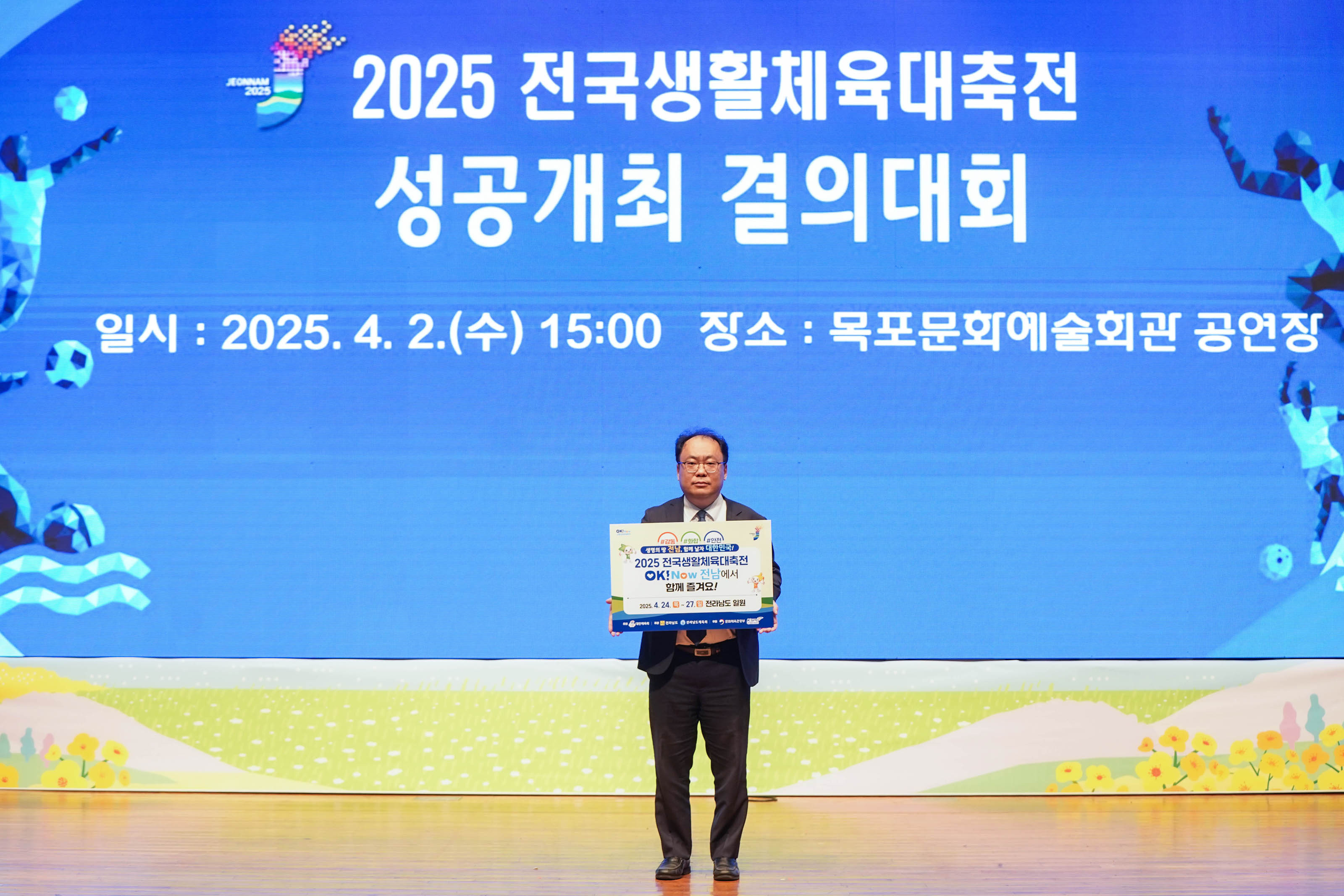 '2025 전국생활체육대축전
성공개최 결의대회
일시:2025.4.2.(수) 15:00 장소: 목포문화예술회관 공연장' 문구가 띄워진 스크린 앞에서 팻말을 든 관계자의 모습