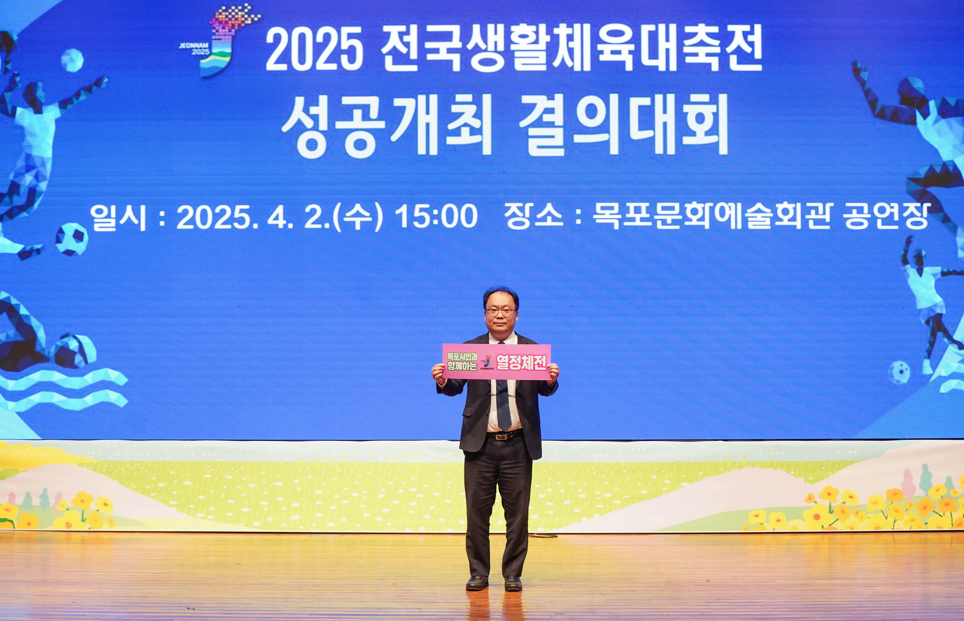 '2025 전국생활체육대축전
성공개최 결의대회
일시:2025.4.2.(수) 15:00 장소: 목포문화예술회관 공연장' 문구가 띄워진 스크린 앞에서 '열정체전' 문구가 적힌 팻말을 든 관계자의 모습