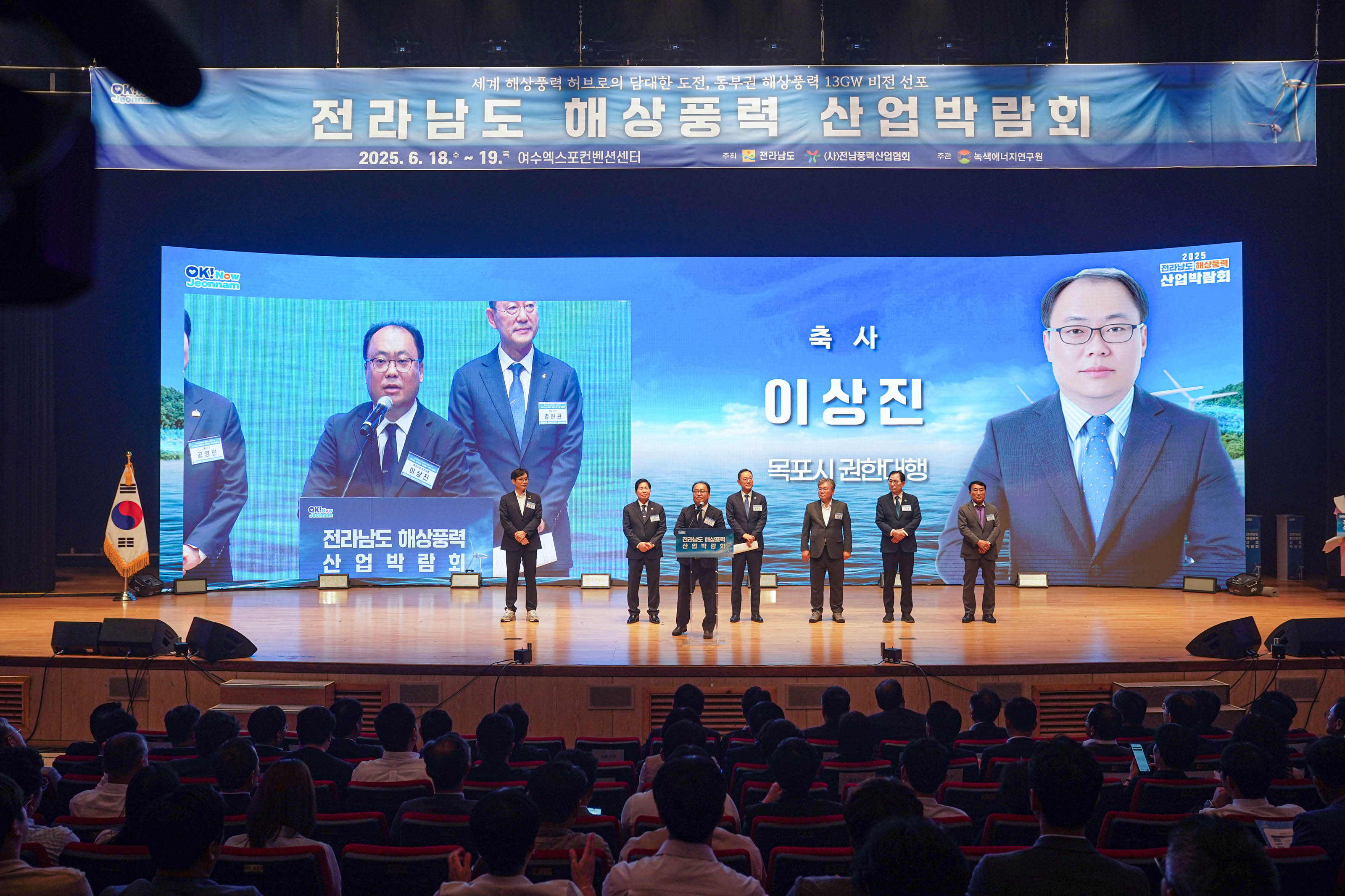 무대 위 대형 스크린 앞에 선 내빈들. 스크린에는 '축사 이상진 목포시 권한대행' 자막과 얼굴 사진이 띄워져 있음.