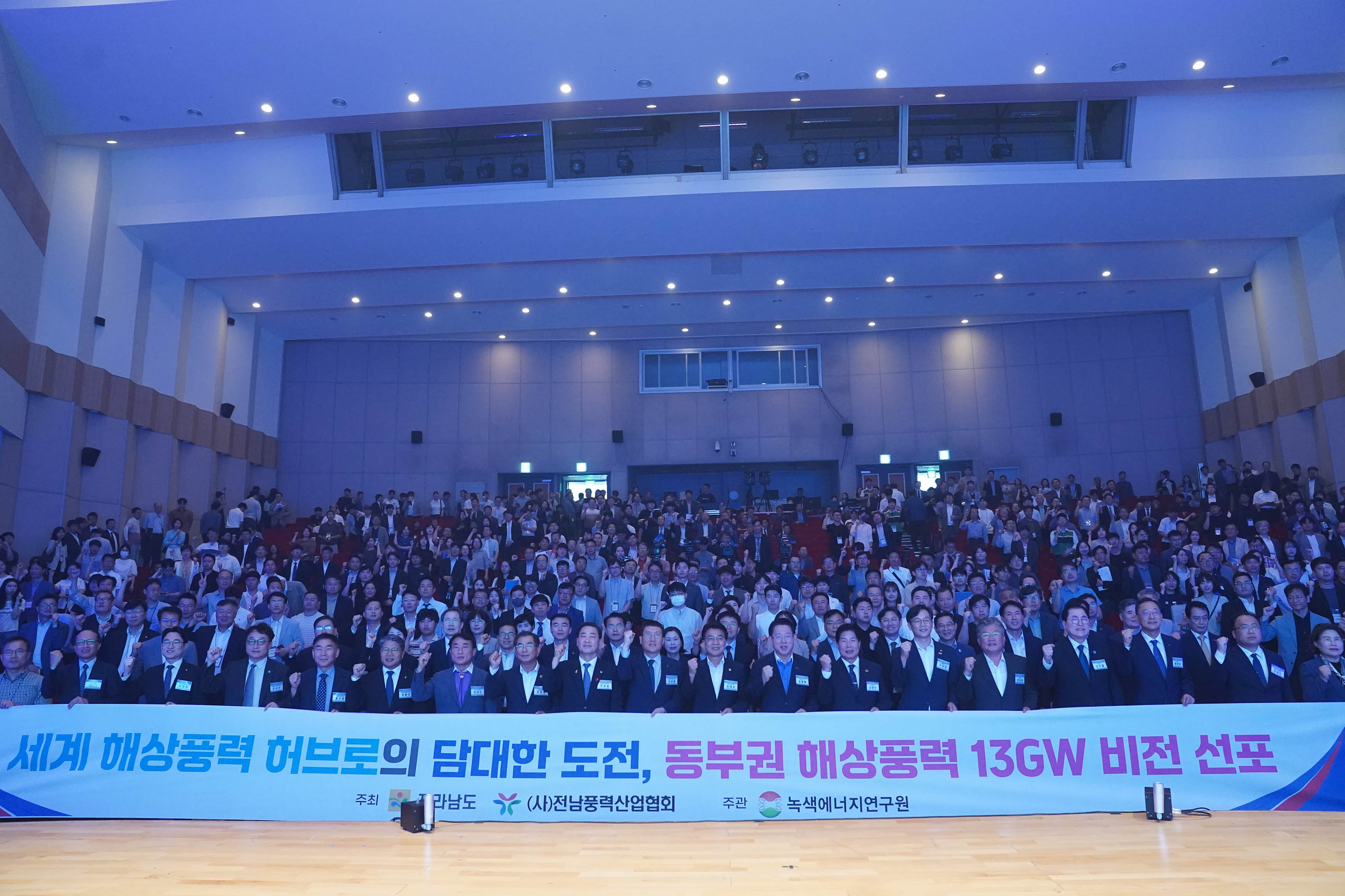 '세계 해상풍력 허브로의 담대한 도전, 동부권 해상풍력 13GW 비전 선포' 현수막을 들고 단체 기념사진을 촬영하는 내빈들과 객석의 참석자들.