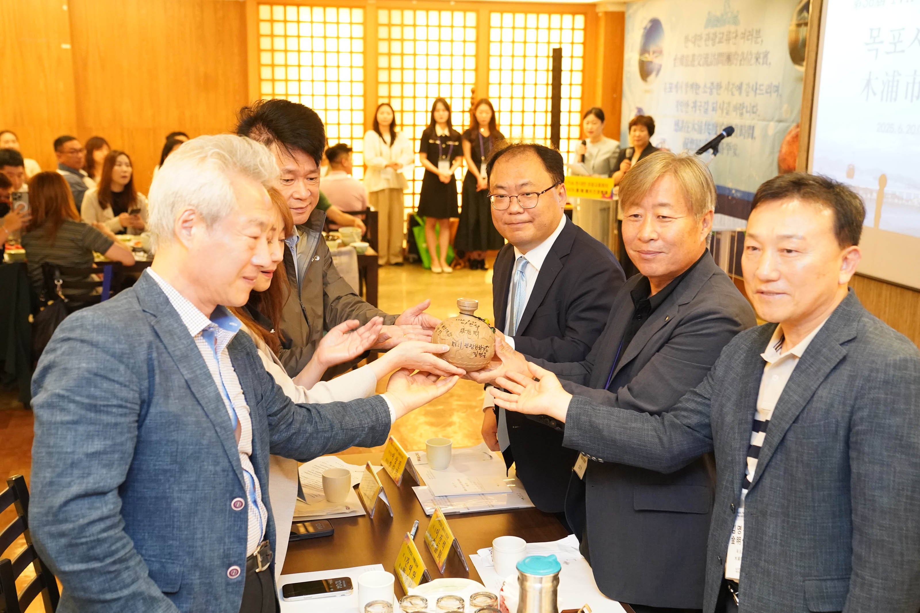 '제38차 KATA/TVA 한·대만 관광교류회의' 현수막 앞에서 참석자들이 기념 서명이 된 도자기 술병을 함께 맞잡고 포즈를 취하는 모습.