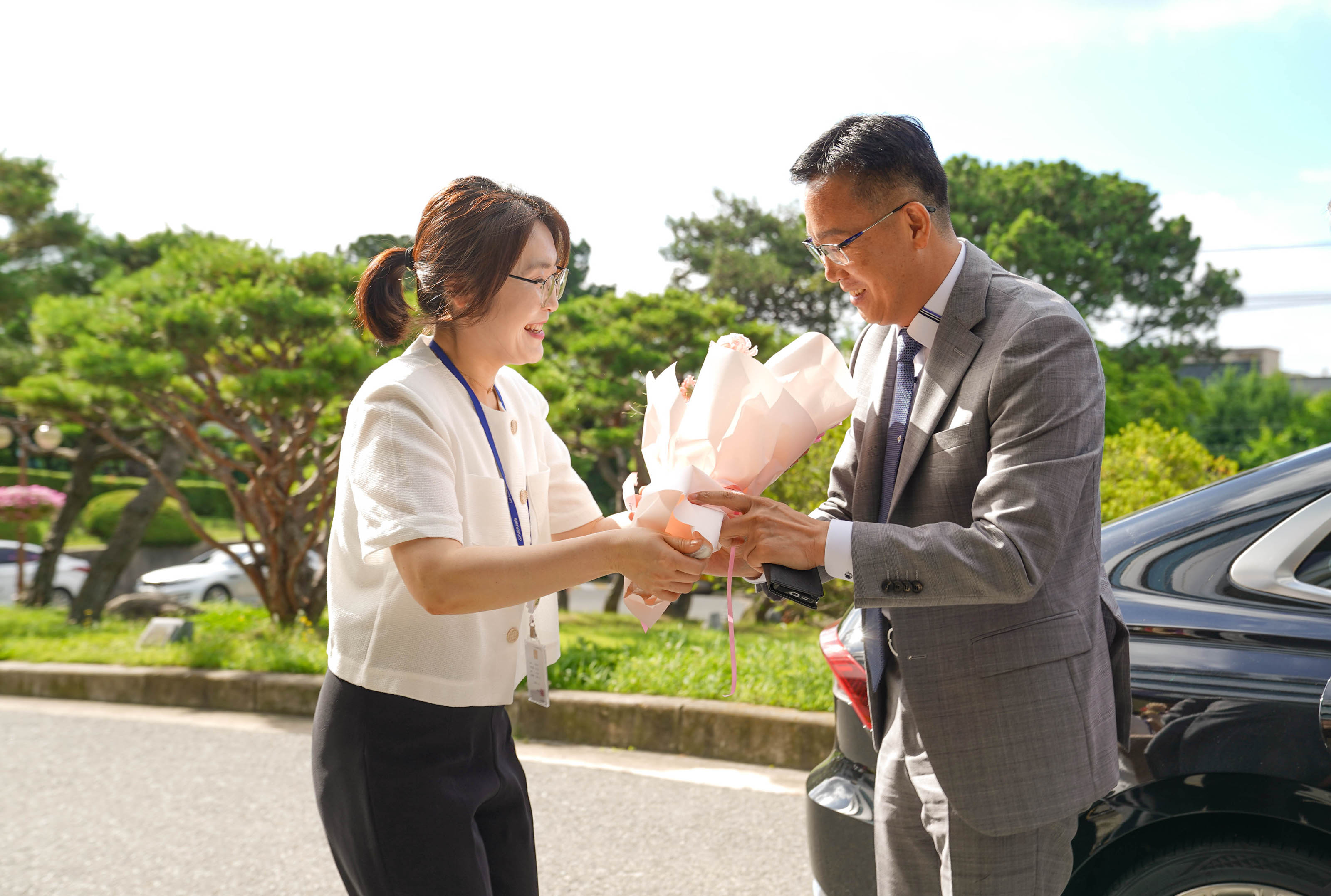 야외에서 흰색 상의를 입은 여성이 회색 정장을 입은 조석훈 목포시 부시장에게 꽃다발을 전달하며 환하게 웃고 있는 모습.