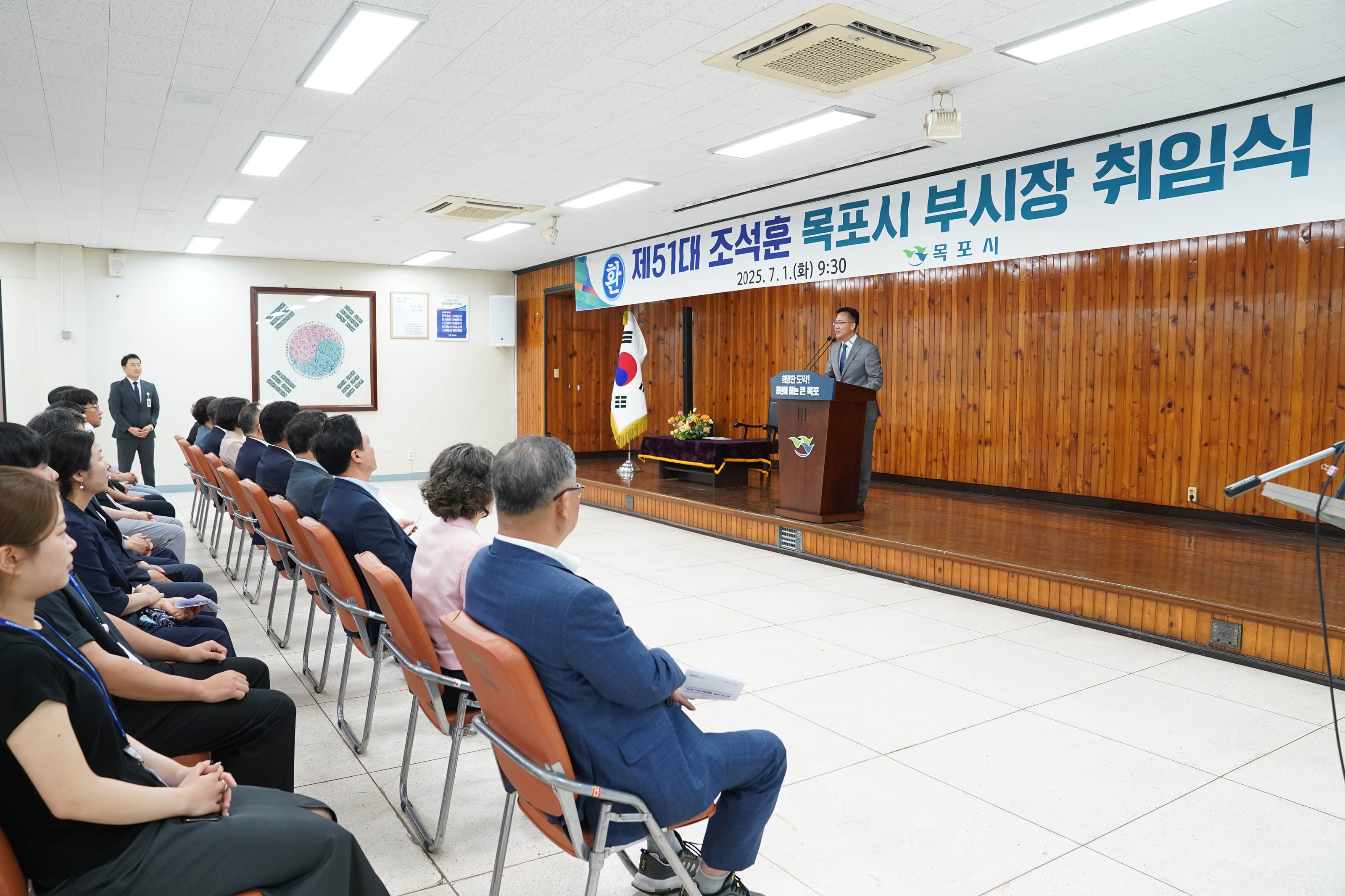 행사장 내부 전경. 정면에 '제51대 조석훈 목포시 부시장 취임식, 2025. 7. 1.(화) 9:30, 목포시'라고 적힌 현수막이 걸려 있고, 조석훈 부시장이 연단에서 취임사를 하고 있는 모습.