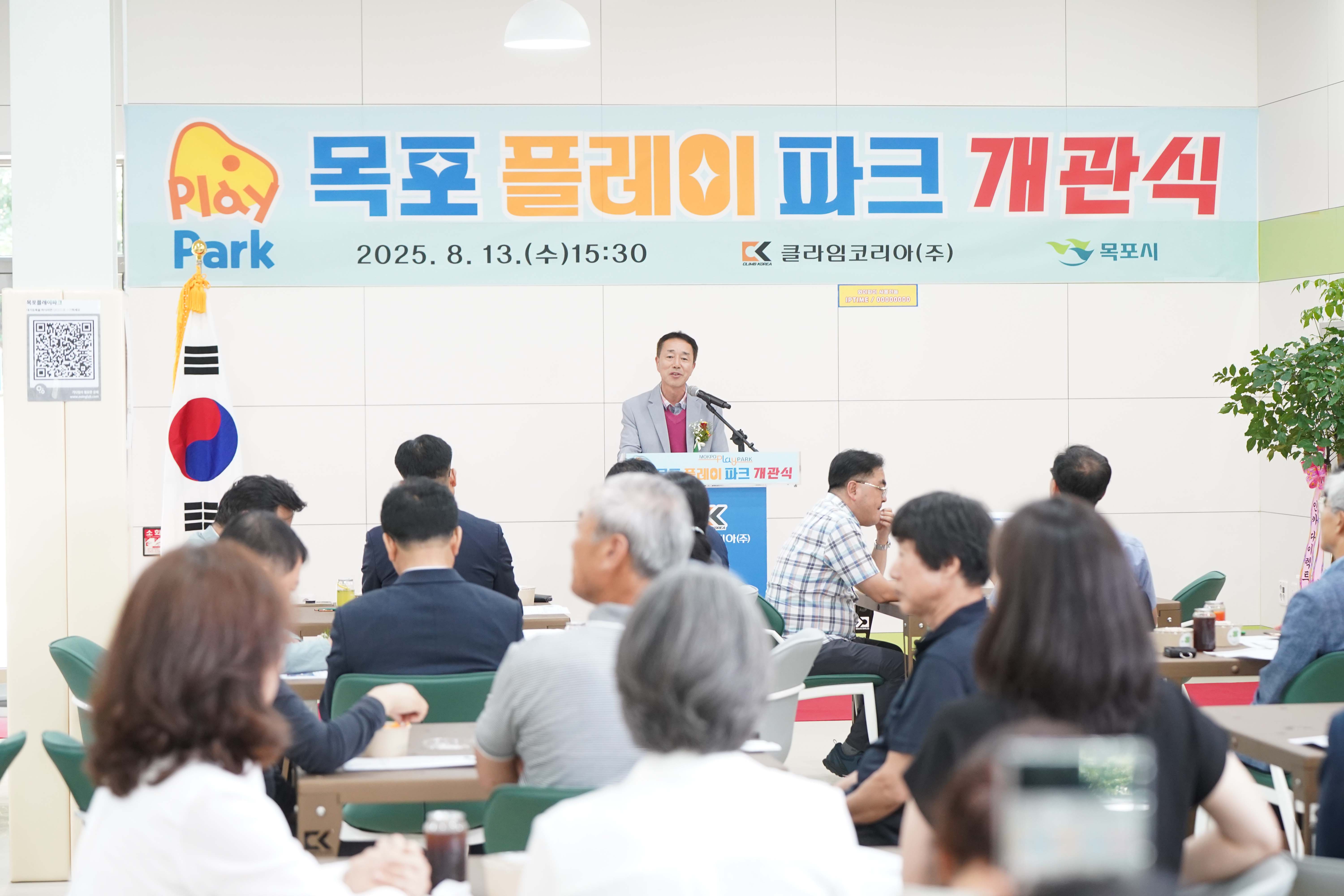 '목포 플레이 파크 개관식' 행사 현장. 2025년 8월 13일 오후 3시 30분 일시와 클라임코리아(주), 목포시 로고가 적힌 현수막 앞에서 한 남성이 축사를 하고 있음.