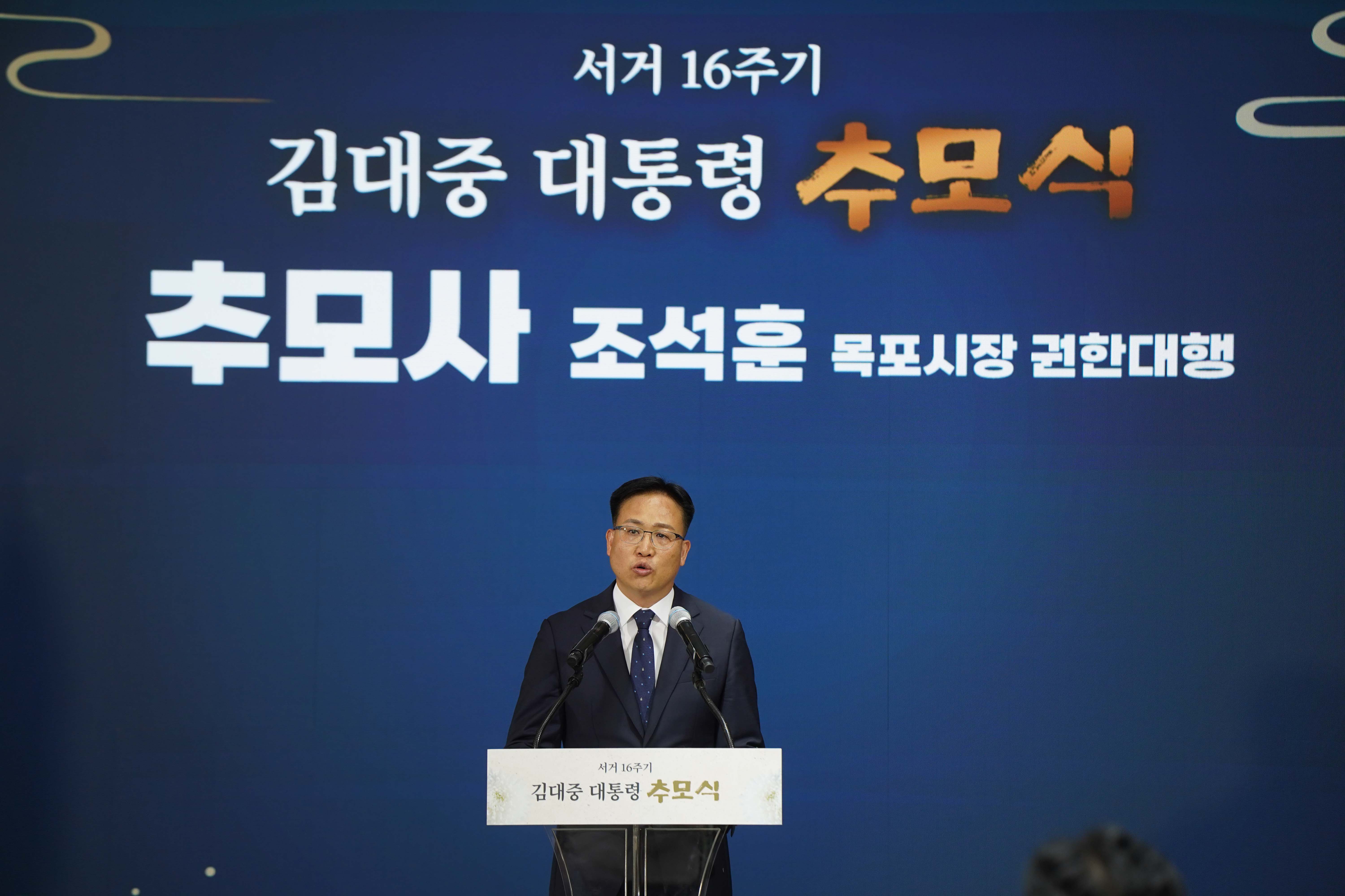 '추모사 조석훈 목포시장 권한대행'이라는 배경 화면 앞에서 발언 중인 모습. 상단에는 '서거 16주기 김대중 대통령 추모식' 문구가 적혀 있음.