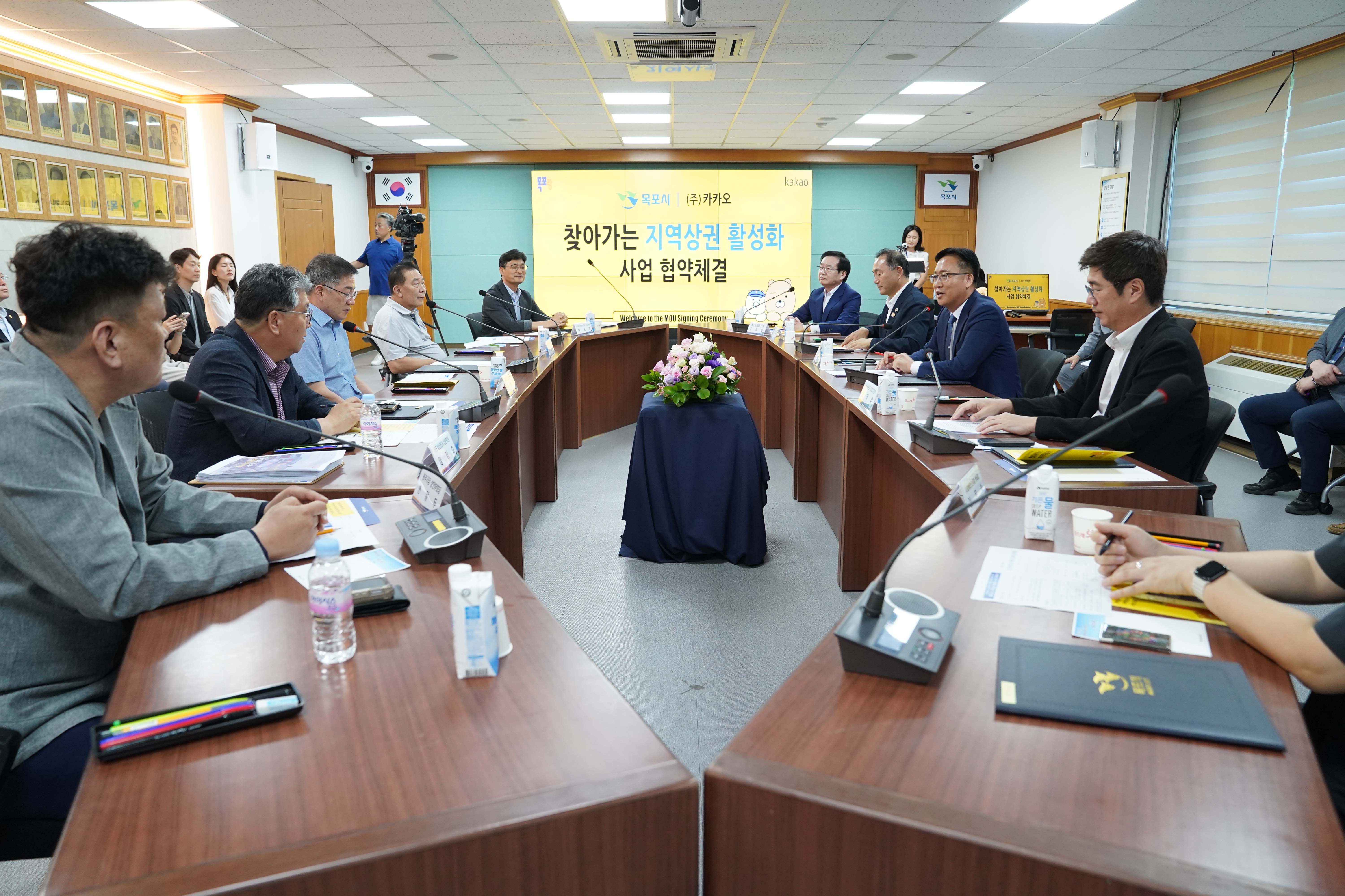 회의실 전면 스크린에 '목포시 | (주)카카오 찾아가는 지역상권 활성화 사업 협약체결' 문구가 띄워져 있고, 'U'자형 테이블에 목포시 관계자들과 카카오 관계자들이 마주 앉아 회의를 진행하는 전경.