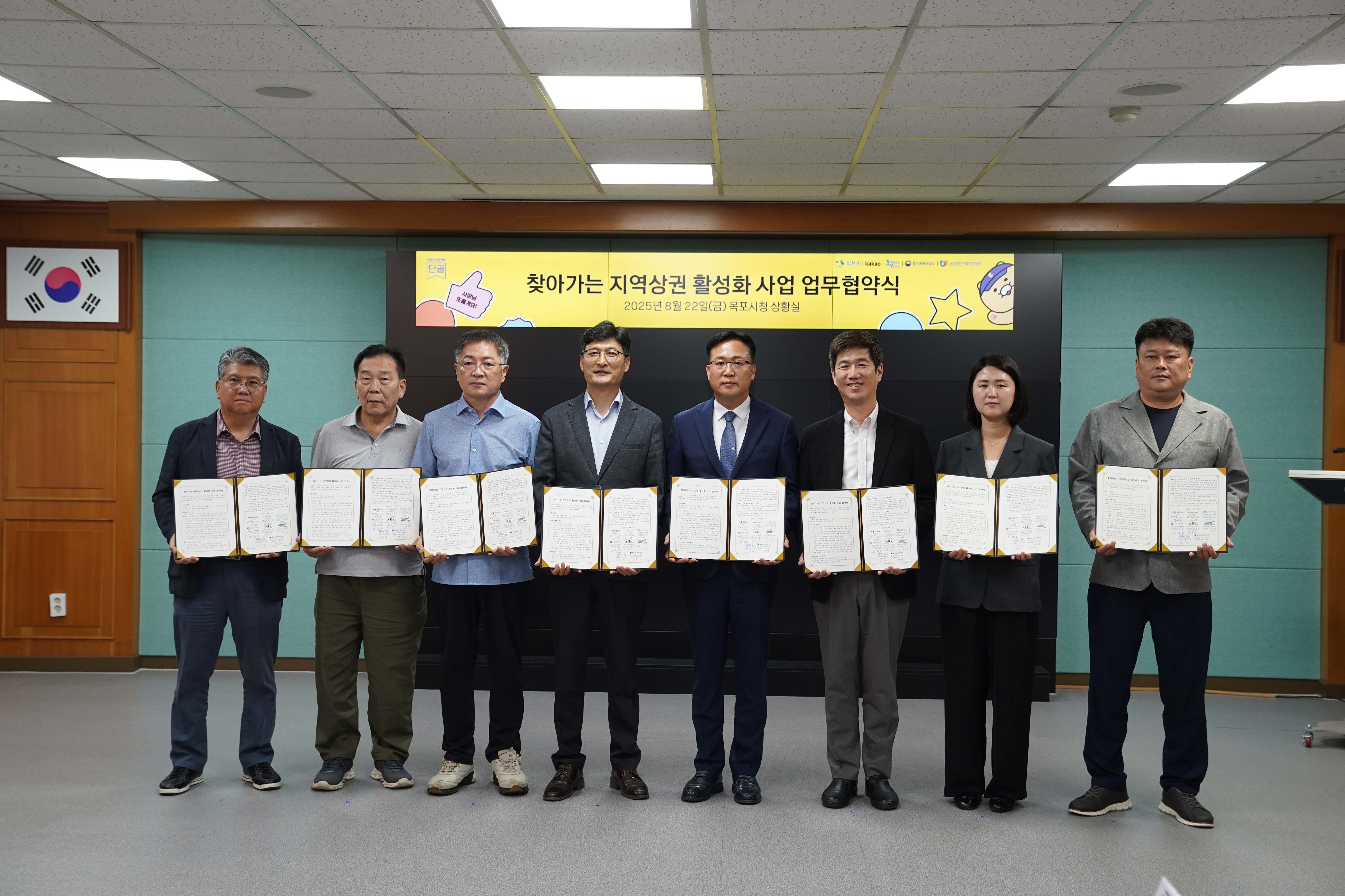 '찾아가는 지역상권 활성화 사업 업무협약식, 2025년 8월 22일(금) 목포시청 상황실' 현수막 아래에서 8명의 협약 참여자들이 각자 서명한 협약서를 들고 기념 촬영을 하는 모습.