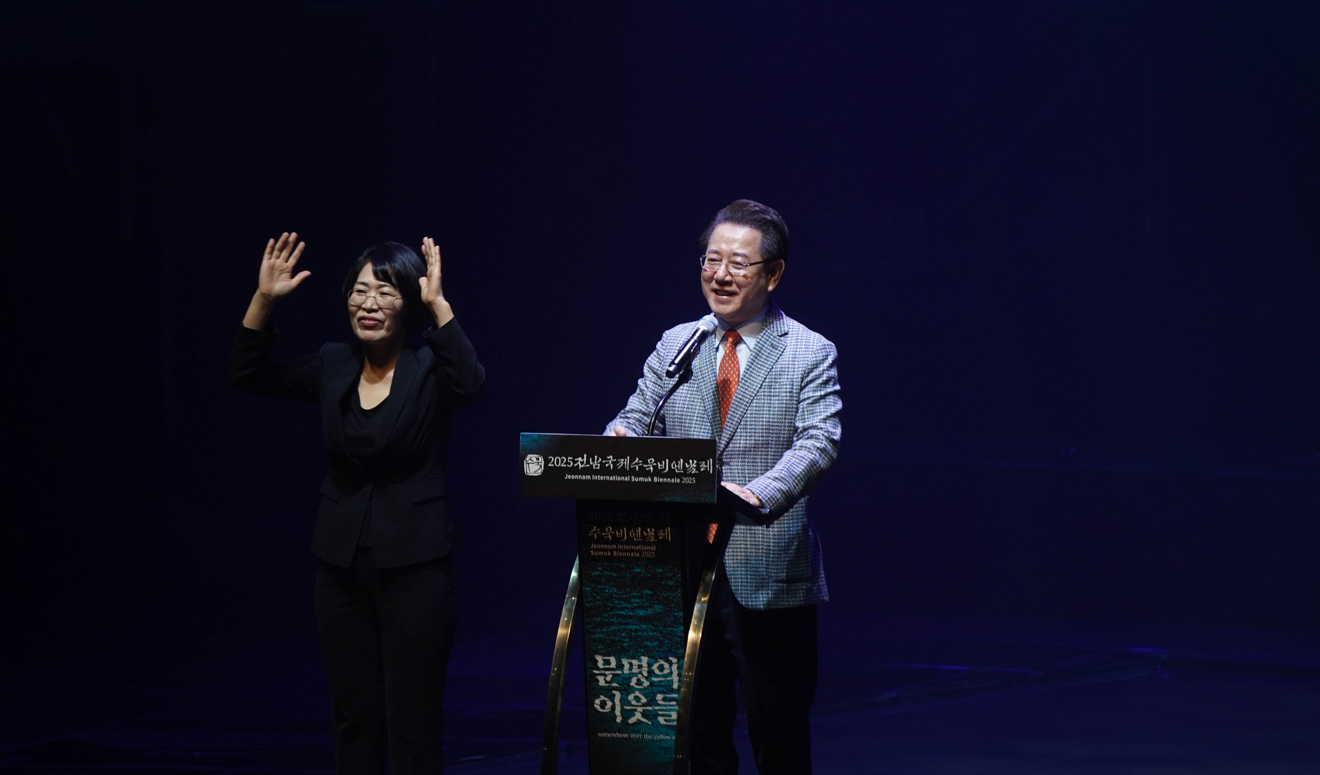 '2025 전남국제수묵비엔날레' 연단에서 김영록 전라남도지사가 환영사를 하는 모습. 연단에는 '문명의 이웃들'이라는 글자가 적혀 있으며, 옆에서는 수어 통역이 진행 중임.