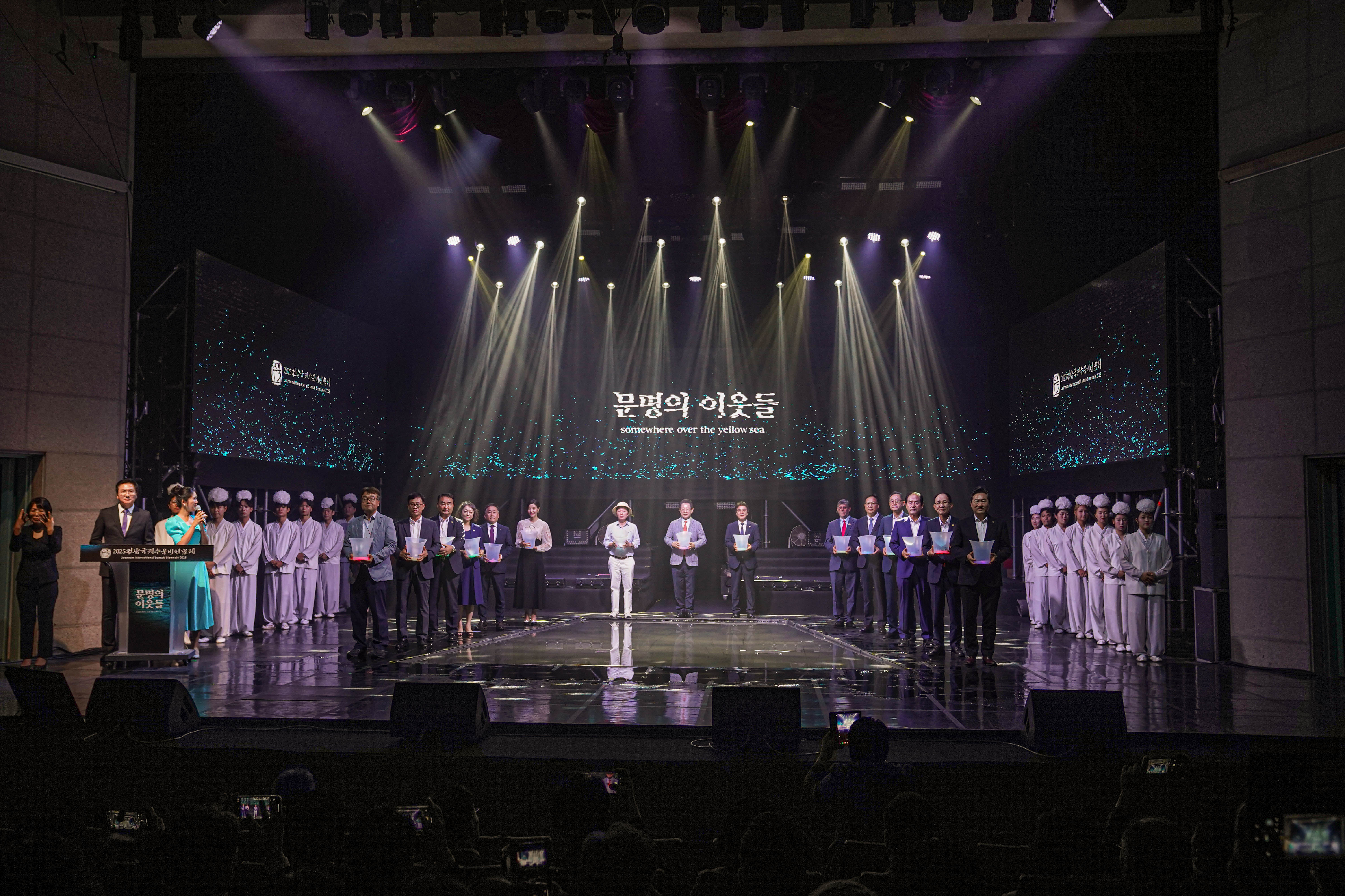 '문명의 이웃들 (somewhere over the yellow sea)'이라는 메인 테마 문구가 적힌 무대에서 내빈들이 LED 조명 버킷을 들고 개막 퍼포먼스를 준비하는 장면.