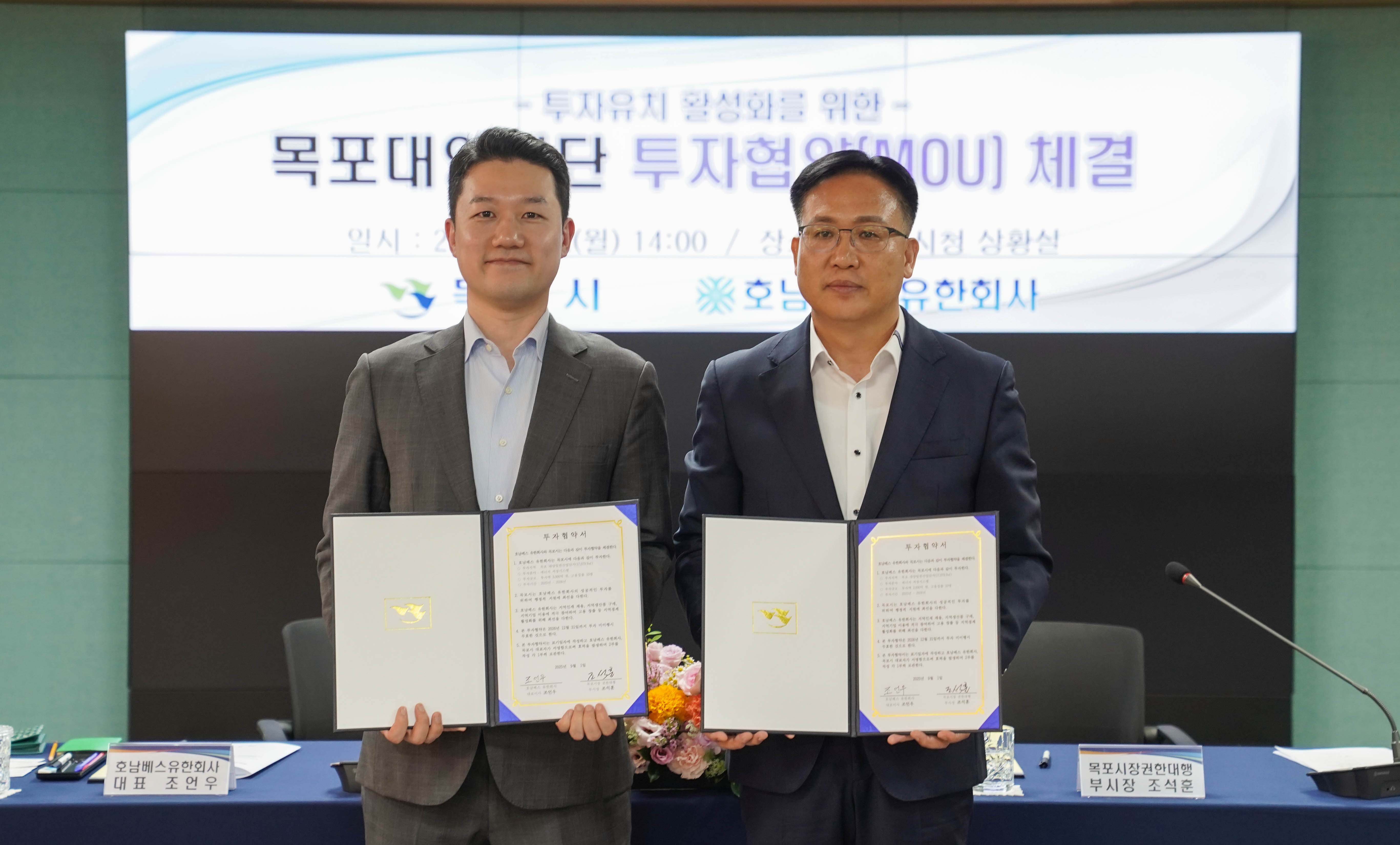 '목포대양산단 투자협약(MOU) 체결' 기념 촬영. 조언우 대표와 조석훈 부시장이 서명을 마친 투자협약서를 각각 펼쳐 들고 정면을 응시하며 서 있는 모습. 뒤쪽 스크린에는 행사 일시와 장소(목포시청 상황실)가 적혀 있음.