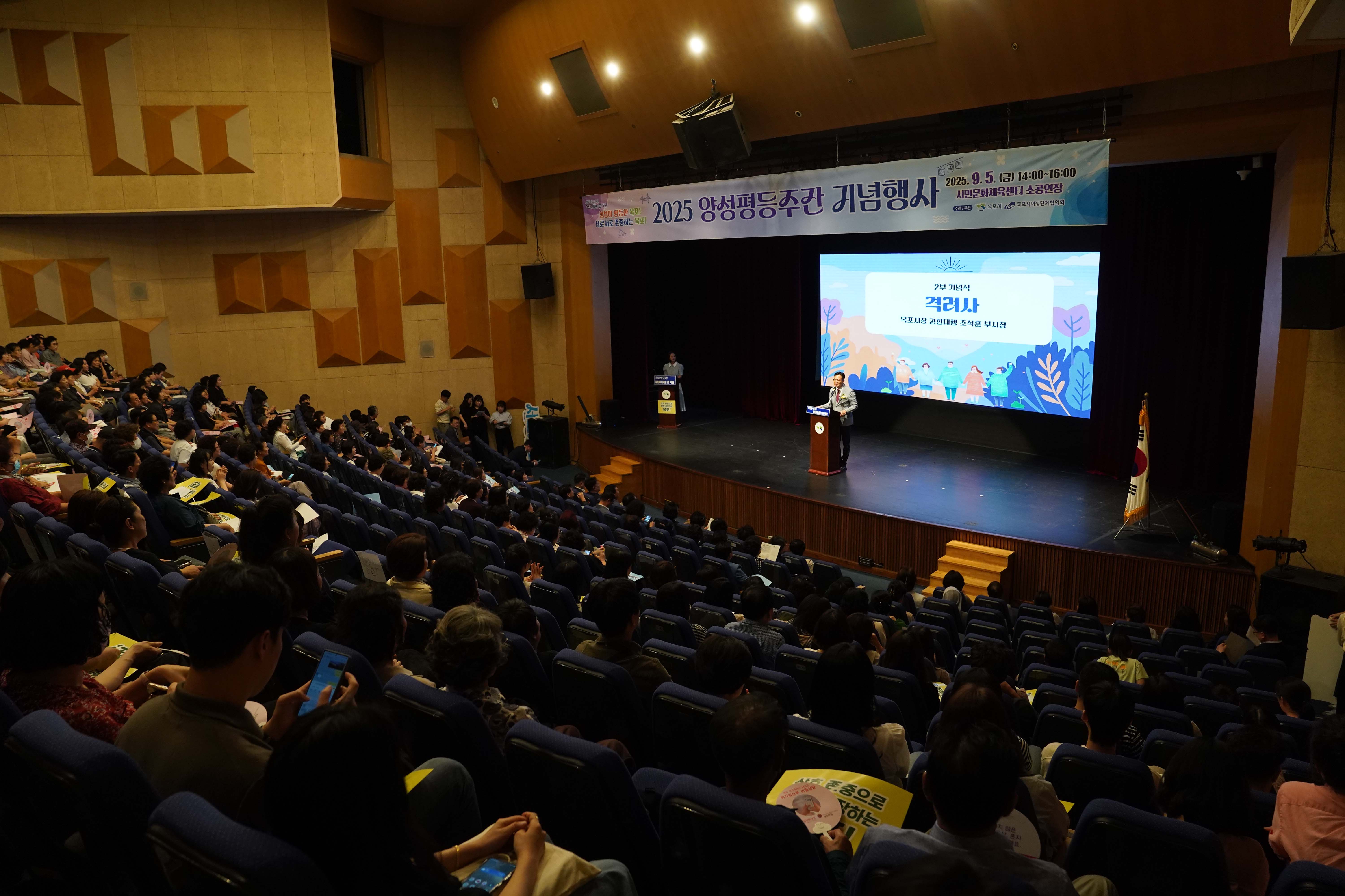 많은 시민이 참석한 공연장 내부 전경. 무대 상단 현수막에는 '2025 양성평등주간 기념행사, 2025. 9. 5.(금) 14:00~16:00, 시민문화체육센터 소공연장'이라고 적혀 있으며, 무대 위 스크린에는 '2부 기념식 격려사 목포시장 권한대행 조석훈 부시장' 문구가 보임.