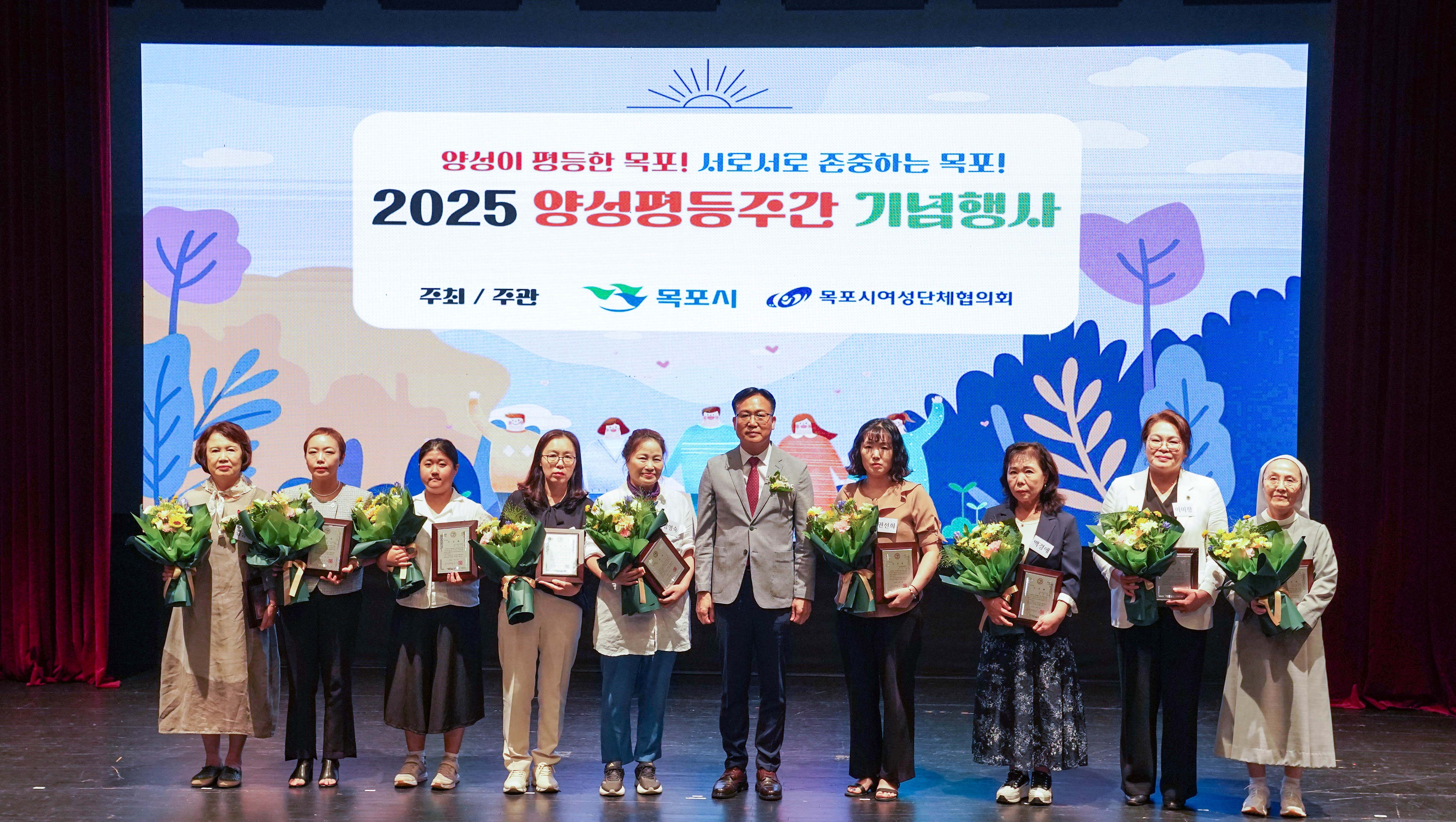 무대 위 스크린에 '양성이 평등한 목포! 서로서로 존중하는 목포! 2025 양성평등주간 기념행사, 주최/주관 목포시, 목포시여성단체협의회' 문구가 보임. 조석훈 부시장과 꽃다발 및 상패를 든 9명의 수상자가 나란히 서서 기념 촬영을 하는 모습.