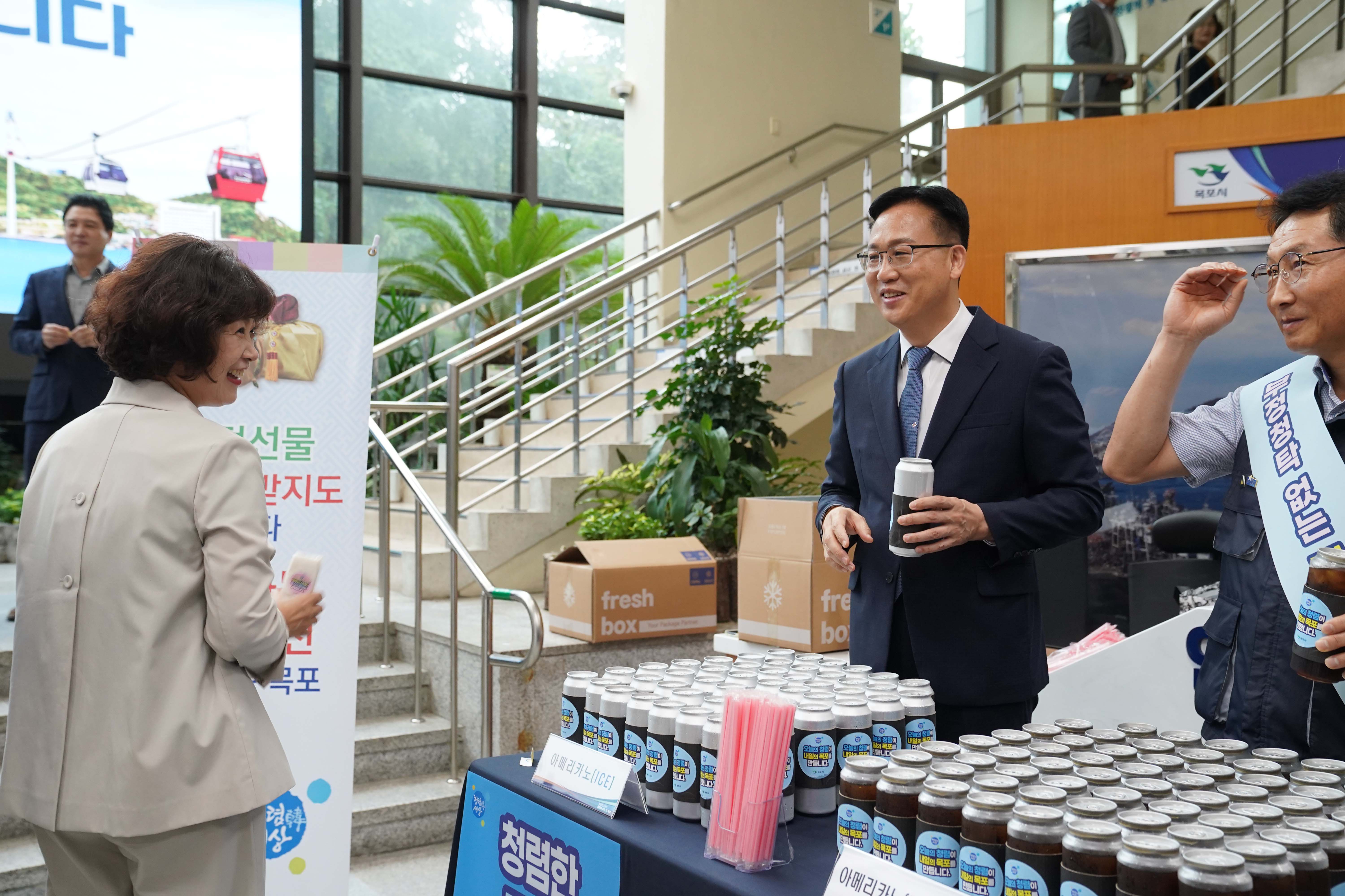 '청렴한 목포' 캠페인 현장에서 관계자가 시민에게 캔커피를 전달하며 대화를 나누는 모습. 옆에는 '명절선물 주지도 받지도 맙시다' 배너가 설치되어 있음.