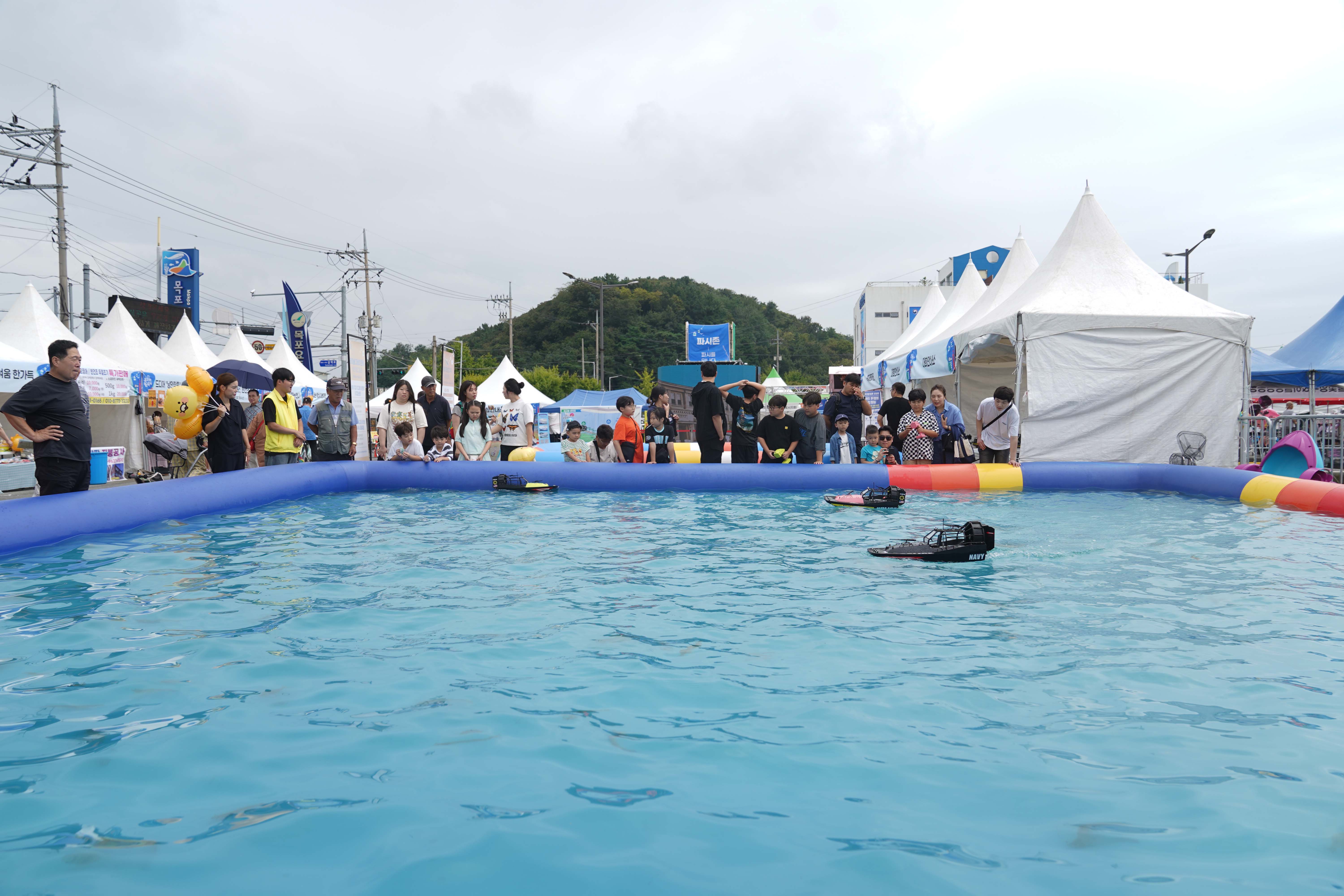 축제장 한편에 마련된 야외 풀장에서 어린이들과 시민들이 모여 무선 조종(RC) 보트 체험을 구경하고 있는 모습.