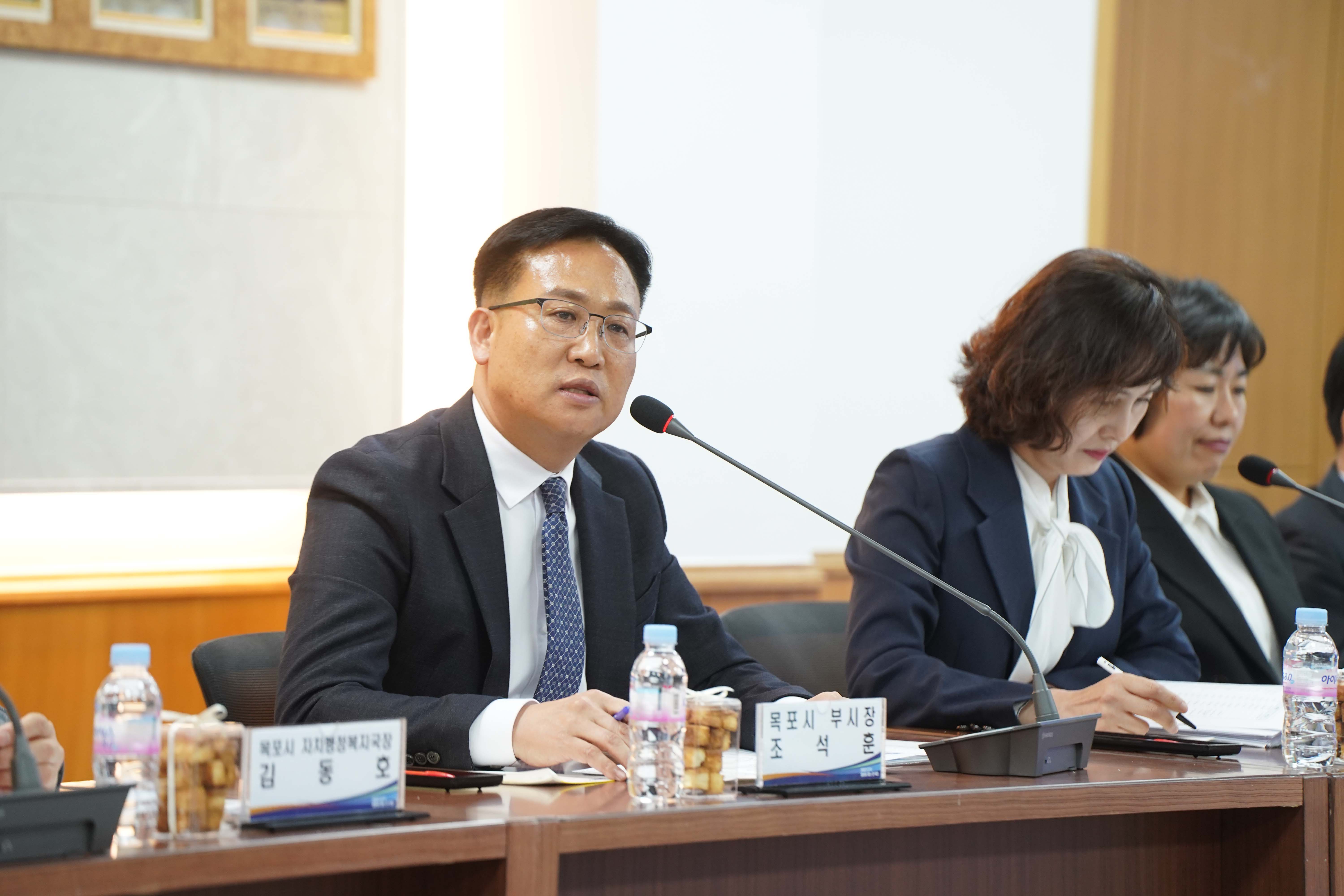'목포시 부시장 조석훈' 명패 뒤에 앉은 조석훈 부시장이 마이크를 통해 발언하는 근접 촬영 사진. 테이블 위에는 회의 자료와 생수병, 간식이 놓여 있음.