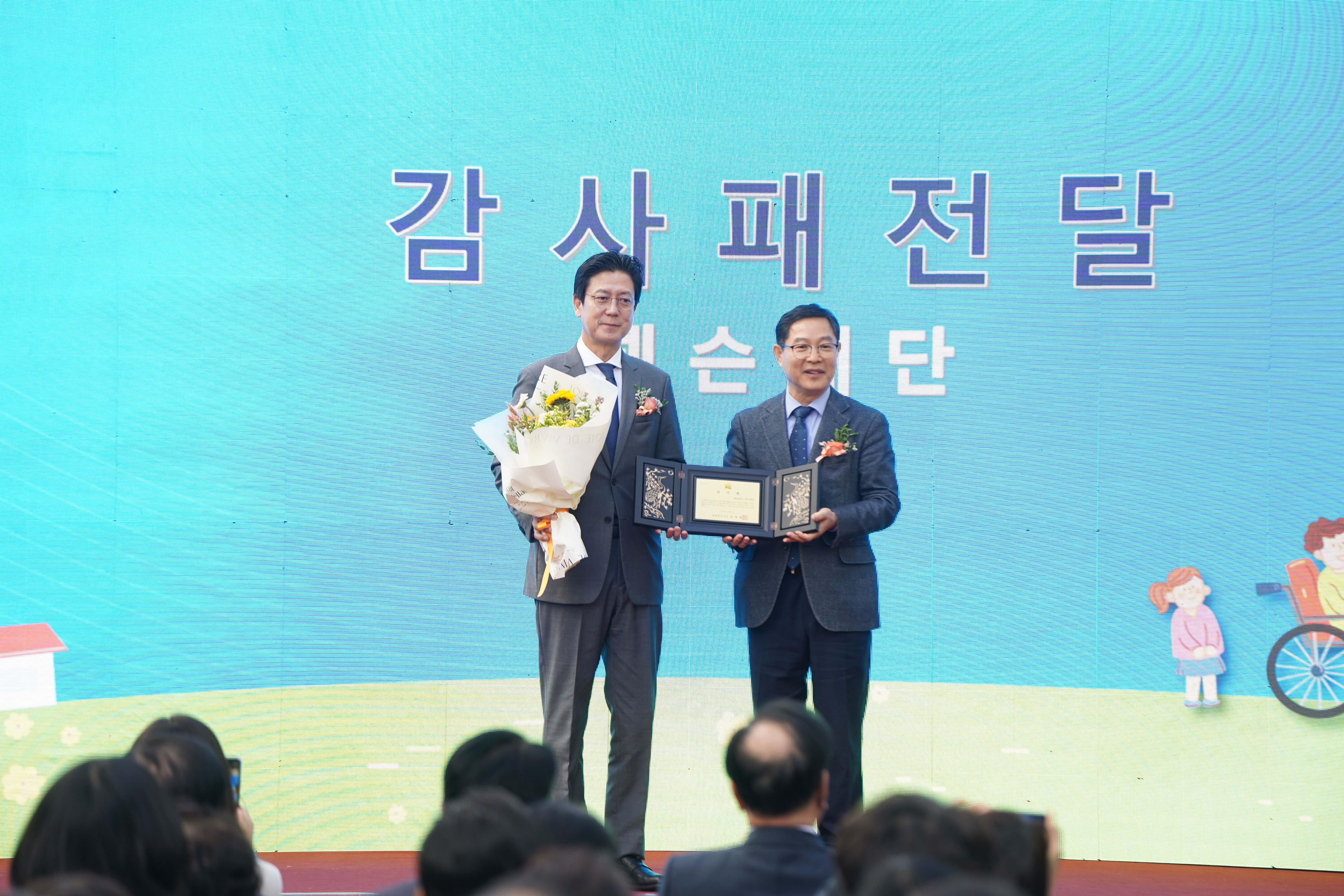 개원식 현장에서 진행된 감사패 전달식. 무대 배경에 '감사패 전달' 문구가 크게 적혀 있으며, 두 내빈이 감사패와 꽃다발을 들고 기념 촬영을 하고 있음.