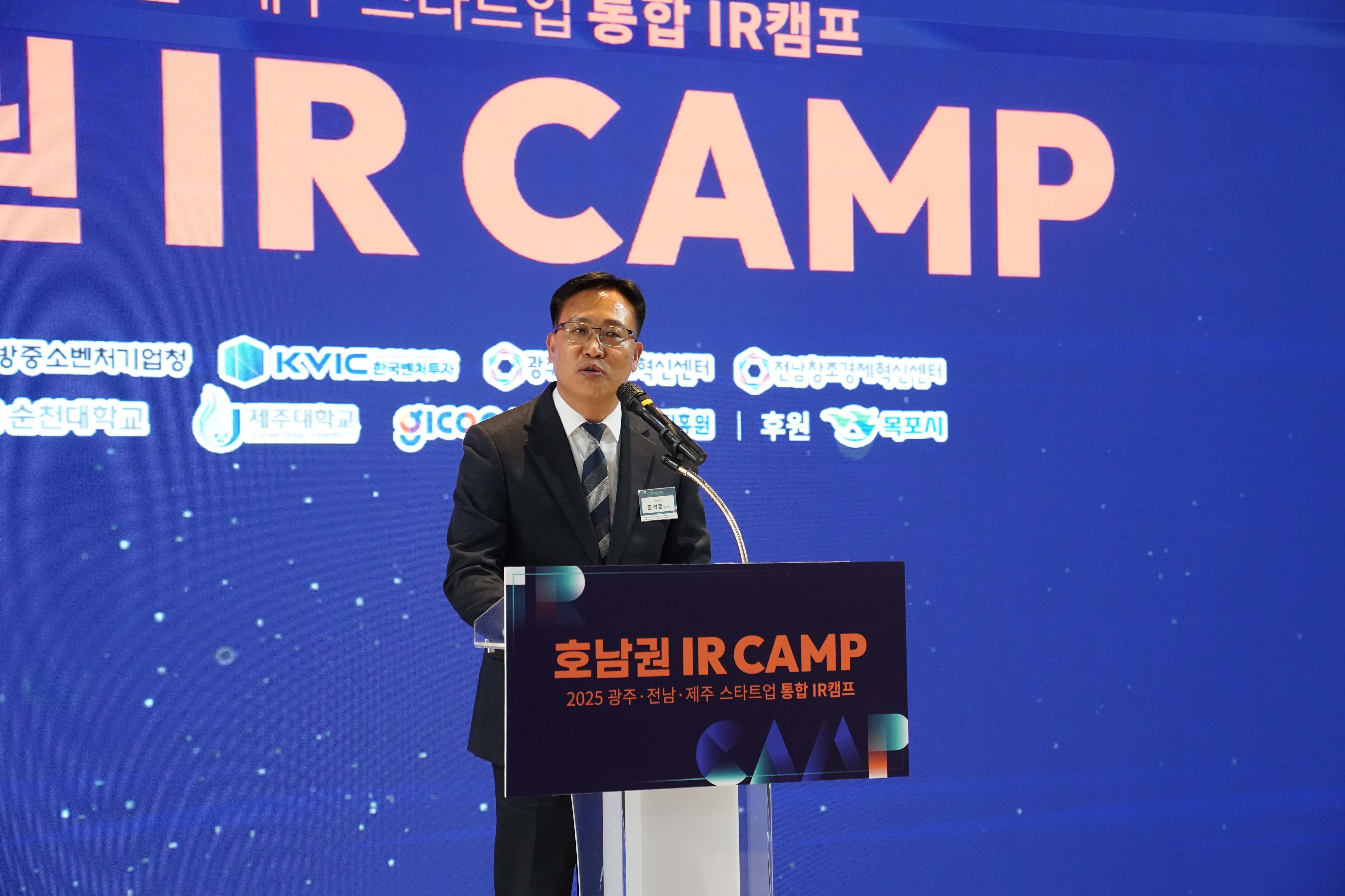 '호남권 IR CAMP' 로고가 적린 연단 뒤에서 조석훈 부시장이 축사를 하는 근접 촬영 모습. 배경에는 다양한 스타트업 지원 기관들의 로고가 나열되어 있음.